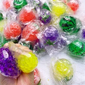 Primer plano de una mano apretando bolas antiestrés de frutas con cuentas de agua de colores