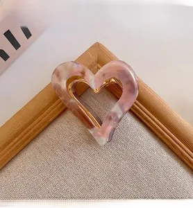 Close-up of heart-shaped hair claw clip with pink marble texture and gold metal frame.