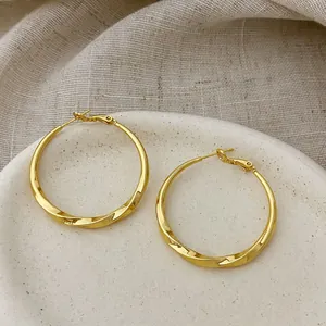 Detailed close-up view of elegant gold plated twisted hoop earrings on ceramic plate