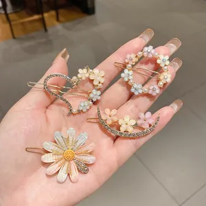 Gros plan de barrettes à fleurs douces avec perles et strass brillants sur une main.