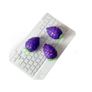 Three purple grape-shaped squeeze toys on a white keyboard for stress relief.