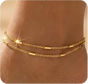 Nahaufnahme einer zwelagigen goldenen Fußkette mit feinen Bar-Anhängern am Knöchel.