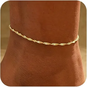 Detailaufnahme einer glänzend vergoldeten, gedrehten Fußkette an einem dunklen Knöchel
