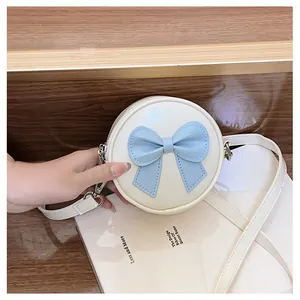 Close-up shot of a cream-colored round girls' crossbody bag with a lovely blue bow detail