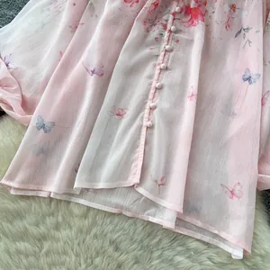 Macro detail of pink chiffon blouse featuring delicate floral patterns and butterfly prints