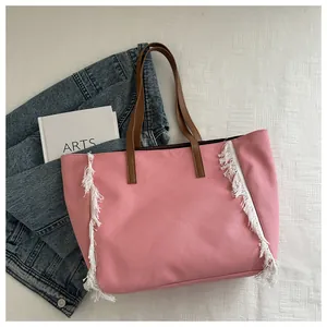 Vue détaillée du sac cabas en toile rose avec des franges blanches et des poignées brunes.