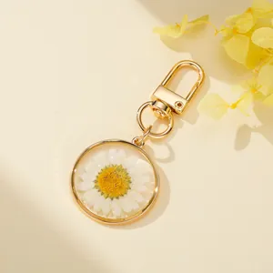 Macro view of a resin keychain featuring a real white dried daisy flower encapsulated in gold