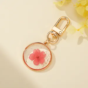 Close-up of clear resin keychain with dried pink flower and gold leaf details.