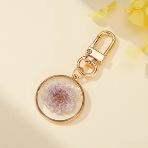 Close-up detail of a resin keychain featuring a purple dried flower and golden metal clasp