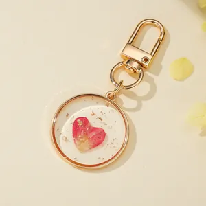 Close-up of a round resin keychain with a pink heart dried flower and gold flakes.