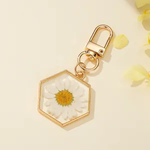 Close-up of hexagonal resin keychain with real dried white daisy and gold hardware.