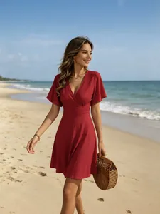 Elegantes rotes Sommer-Minikleid mit V-Ausschnitt für Damen am sonnigen Strand mit Bambustasche