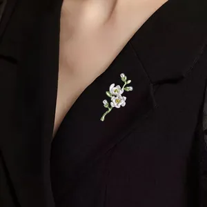 Close-up detail of an elegant white floral brooch with small pearls on a black blazer