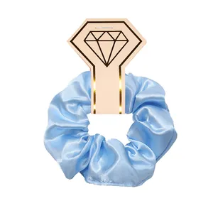 Detailed macro view of a shiny light blue satin scrunchie with elegant diamond card packaging