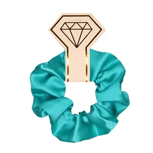 Macro detail of teal satin scrunchie on a stylish diamond-shaped pink display card
