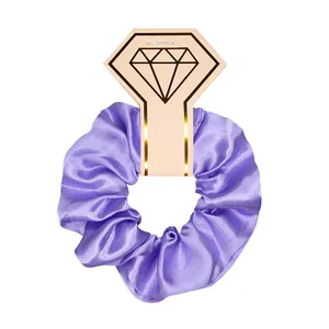 Close-up detail of a purple satin scrunchie presented on a diamond-shaped paper card tag