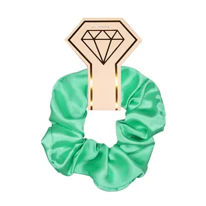 Green shiny satin hair scrunchie presented on a diamond-shaped cardboard display tag.