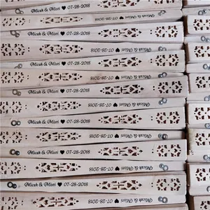Close-up of personalized wooden folding fans with intricate hollow patterns for weddings