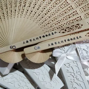 Close-up of hollow-out folding wooden fan with white gift box and ribbon