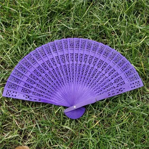 Classical elegant purple hollowed-out folding wooden fan displayed on a lush green grass background.