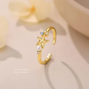 Vue détaillée d'une bague étoile de mer dorée avec perle et éclats de zircon bleu