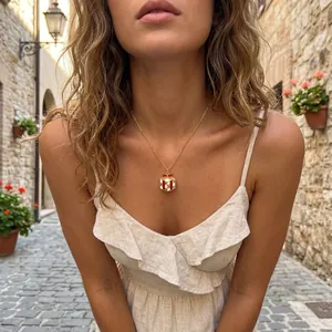 Detail view of a golden Christmas gift box pendant necklace worn outdoors by a model