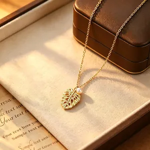 Detailed macro view of brushed gold monstera leaf pendant necklace featuring a pearl accent