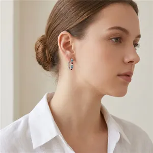 Detailed view of geometric U-shaped stainless steel earring with colored zircons on model ear