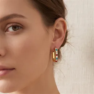 Close-up view of gold U-shaped hoop earrings with colorful zircon stones worn by a model