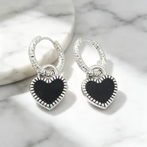 Vue détaillée de boucles d'oreilles cœur en émail noir sur une surface en marbre