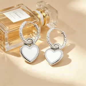 Détail des boucles d'oreilles créoles avec pendentifs en forme de cœur blanc texturé.