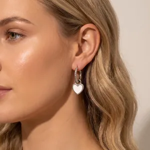 Vue détaillée d'une boucle d'oreille cœur en émail blanc sur l'oreille d'un modèle
