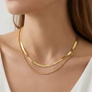 Gros plan d'un collier doré superposé avec chaîne serpent et chaîne torsadée.