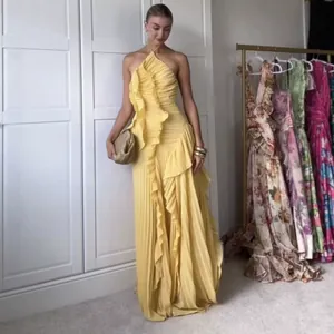 Elegant yellow pleated ruffled halter evening gown worn by a model in a dressing room.