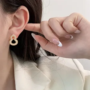 Close-up of elegant gold gourd stud earrings with pavé crystals on Asian model.