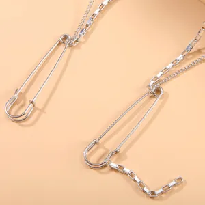 Close-up detail of silver metallic long chain brooch featuring punk style safety pins