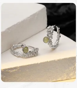 Close-up of S925 sterling silver flower earrings with green gemstone on textured stone