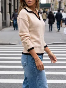 Close-up detail of women's beige knit sweater with black contrast collar and gold buttons.