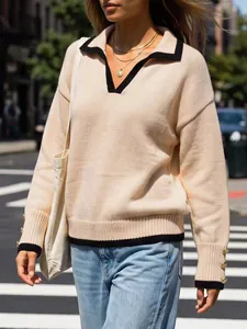 Detail view of a beige knit pullover featuring a black polo collar and gold button cuffs.