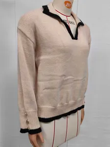 Detail of beige knit sweater with black contrast lapel collar and gold button cuffs.