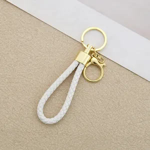Close-up of white braided leather rope keychain with shiny gold metal ring.