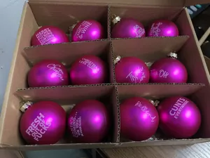 Detail showing twelve pink matte Christmas ball ornaments with offensive text in a storage box