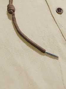 Detailed close-up of a brown woven drawstring with metal tip on a beige shirt