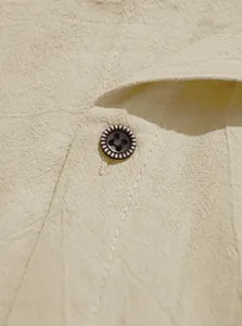 Close-up of beige linen fabric texture and dark brown button detail on men's shirt