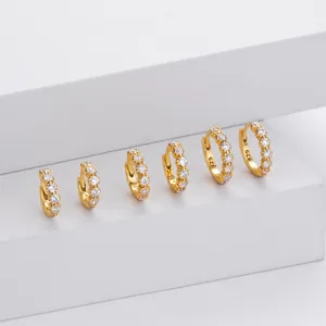 Detailed shot of graduated gold CZ huggie hoop earrings on minimalist white geometric blocks