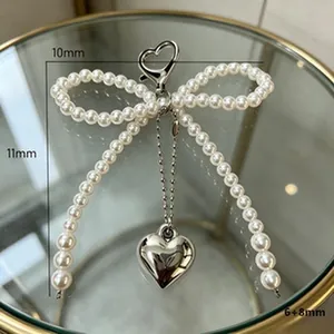 Dettaglio di un ciondolo per borsa a fiocco in perle fatto a mano con cuore in argento.
