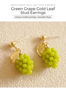 Macro detail view of handmade green grape stud earrings with delicate golden leaf