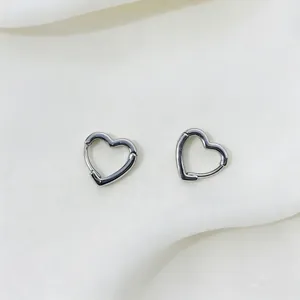 Detailed view of silver heart-shaped huggie earrings on soft white fabric background