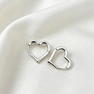 Macro view of minimalist silver hollow heart-shaped hoop earrings on elegant white silk