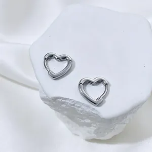Close-up of minimalist silver hollow heart-shaped hoop earrings on a white stone display.